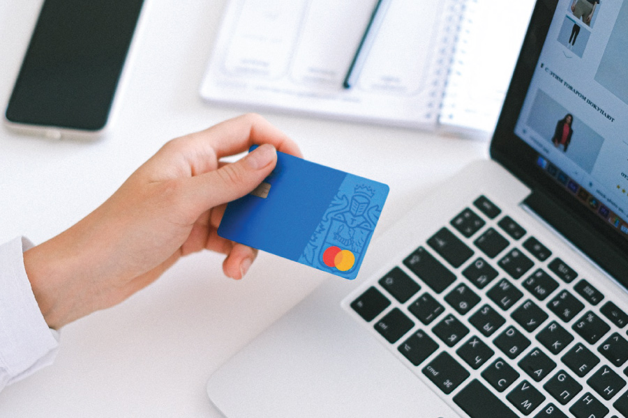 A hand holding a credit card above a laptop