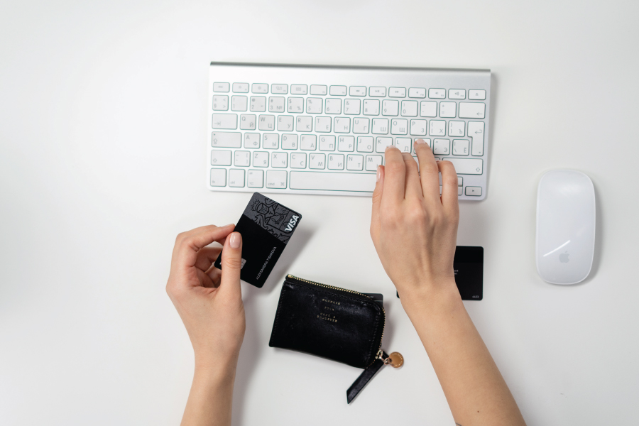 Hands typing on a computer keyboard. One hand is holding a visa credit card