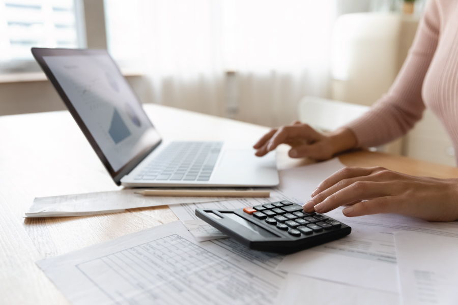 A woman at a desk filled with papers, a calculator, a pencil, and a laptop