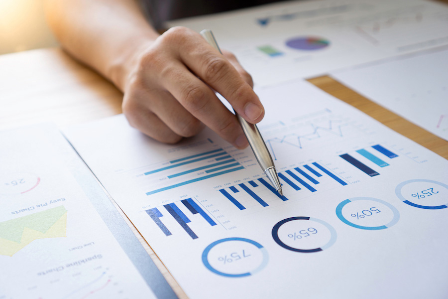 A piece of paper filled with graphs. A hand holding a pen is pointing to one graph.