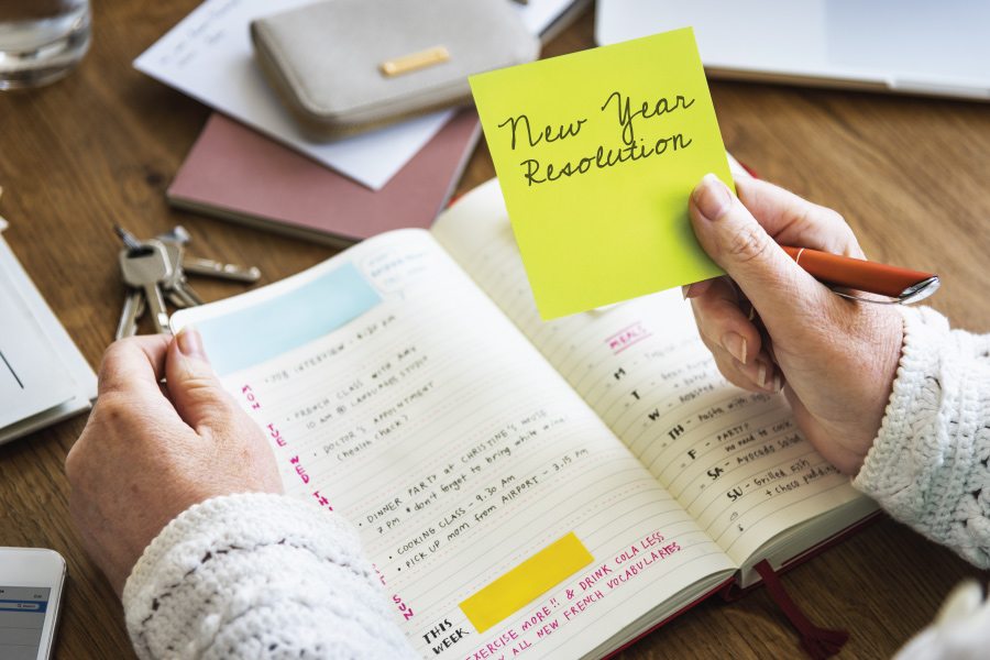 A person holds a notebook open and a sticky note says, "New Year Resolution"