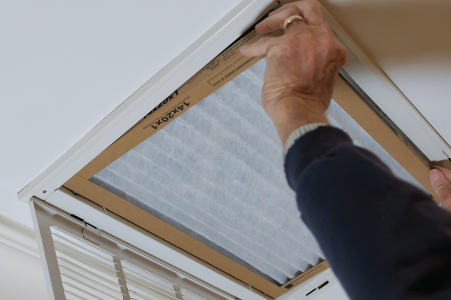 Two hands reaching into a vent to install a furnace filter