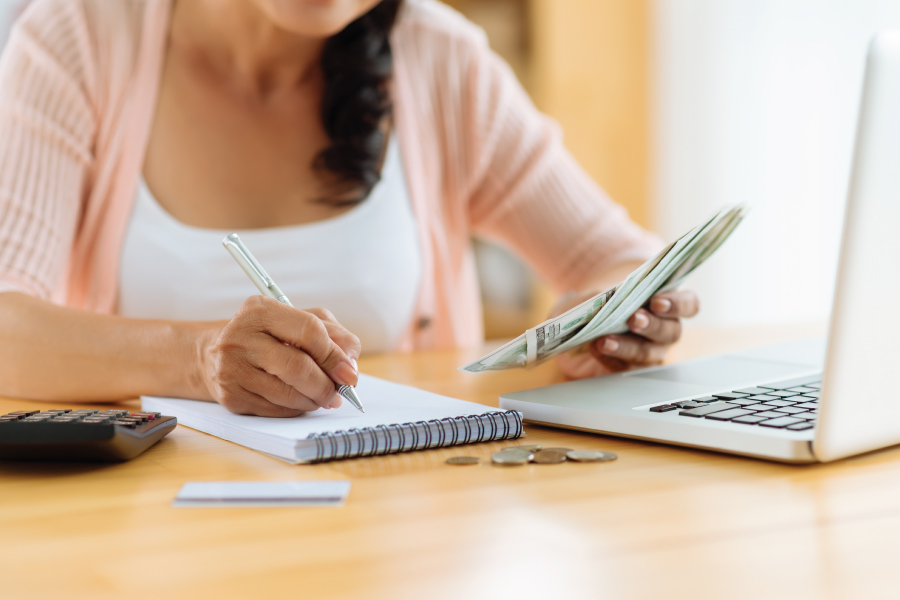 A woman at a desk with a handful of cash. She is writing in a notebook.