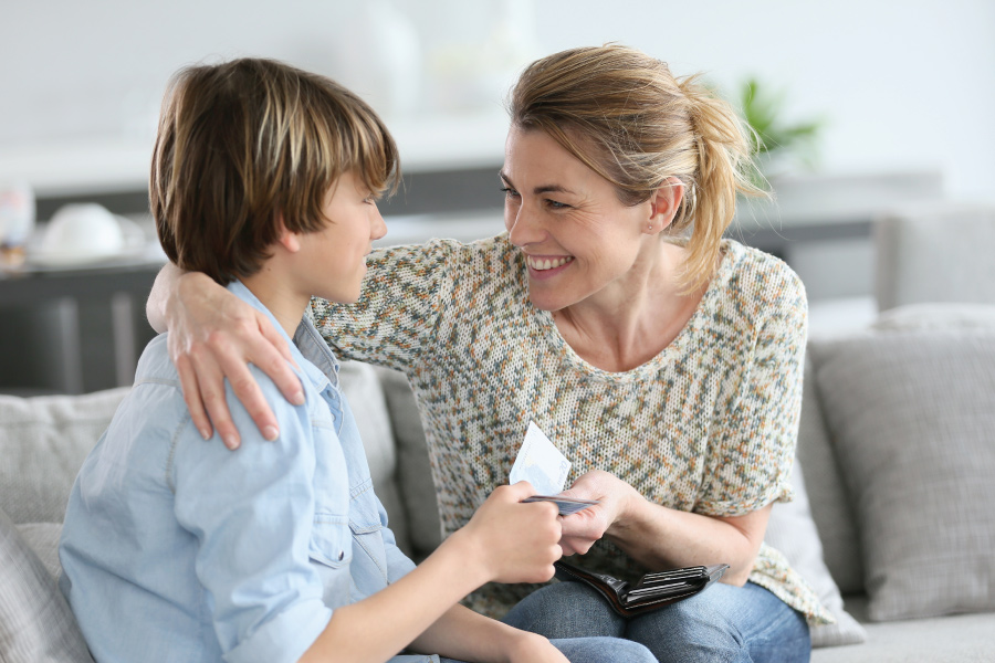 A woman and a child on a couch. The woman is smiling and giving the child a $20 bill.