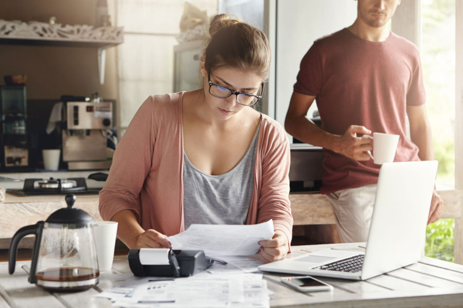 woman sitting at her kitching counter drinking coffee and paying bills