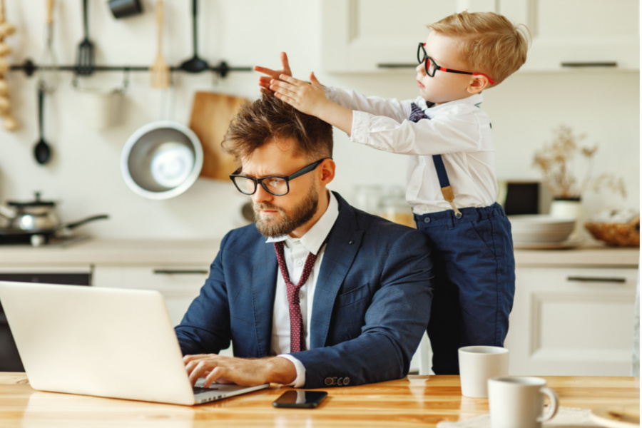 corporate man working on a computer while his son plays with his hair