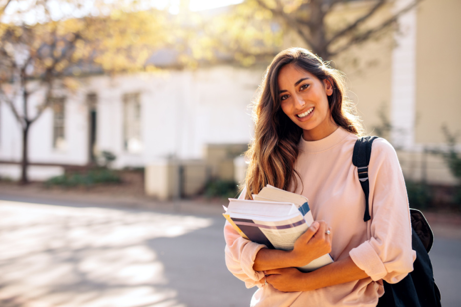young woman holding text books on college campus
