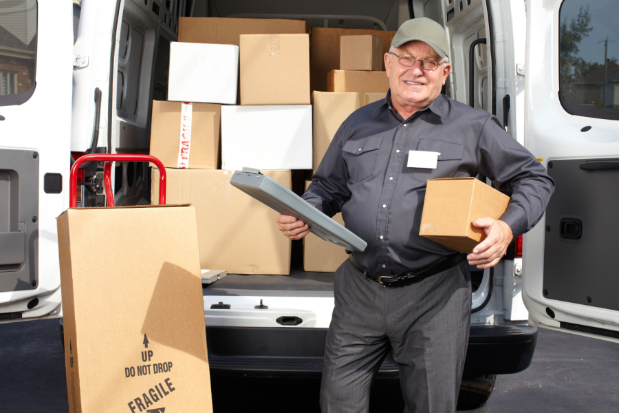 reliable senior delivery man standing in front of truck filled with packaged to be delivered