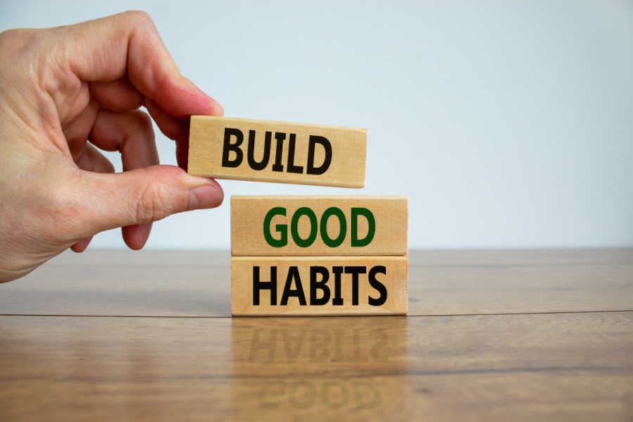 Man placing 3 blocks on a wooden table; each has a word on it: Build, Good, Habits.