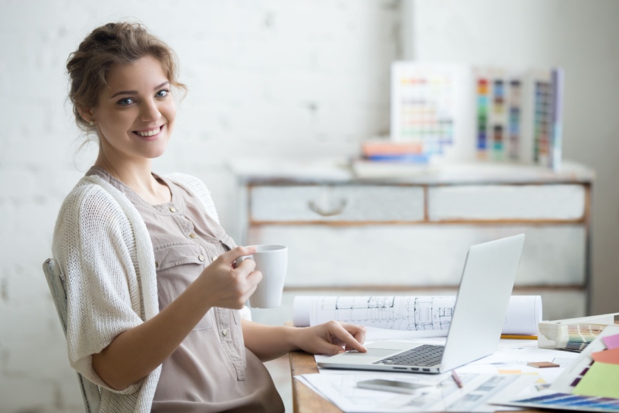 young female architect sitting at her computer with papers on her desk and a coffee in her hand