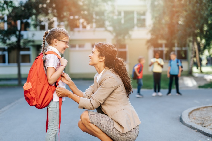 working mother kneeling down to say goodbye to her daughter at school drop off